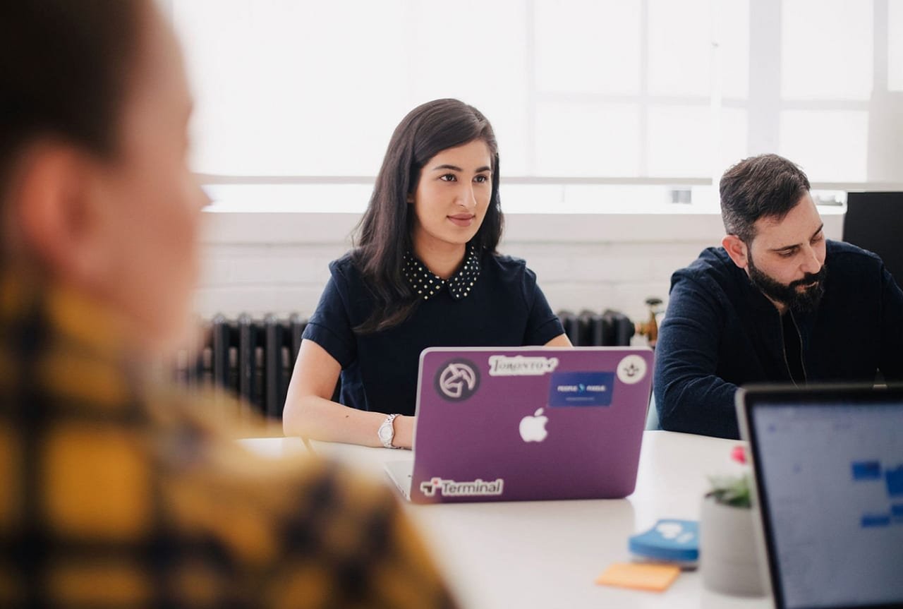 People sitting around a table in a meeting with a laptop on the table. 